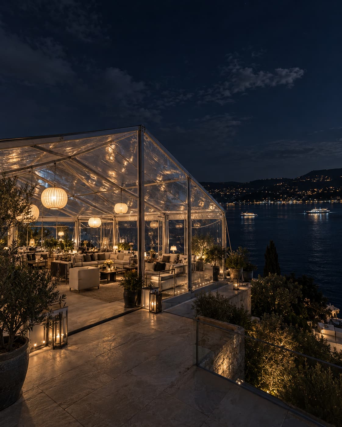 Deniz kenarı terasında tamamen şeffaf çadır, gece; içeride lounge oturma ve kâğıt fenerler, karşı kıyıda ışıklar — konsept görsel